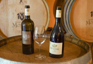 Dos botellas de vino Domaine de Montine y una copa sobre un barril en Flower Camping la Pinède, Auvergne-Rhône-Alpes.