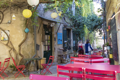 Terrasse de café extérieure avec tables et chaises roses, verdure et ambiance de vacances en Auvergne-Rhône-Alpes.