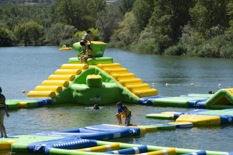 Children play on an inflatable water park on a lake near Die, Auvergne-Rhône-Alpes, France, with trees around.