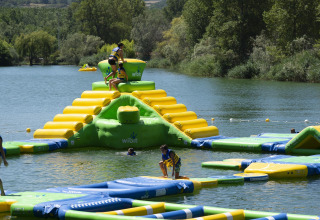 Des enfants jouent sur un parc aquatique gonflable sur un lac près de Die, Auvergne-Rhône-Alpes, France, entouré d’arbres.