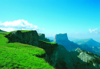 Scogliere verdi e prati nei dintorni di Die, Auvergne-Rhône-Alpes, Francia, con montagne e cielo azzurro sullo sfondo.
