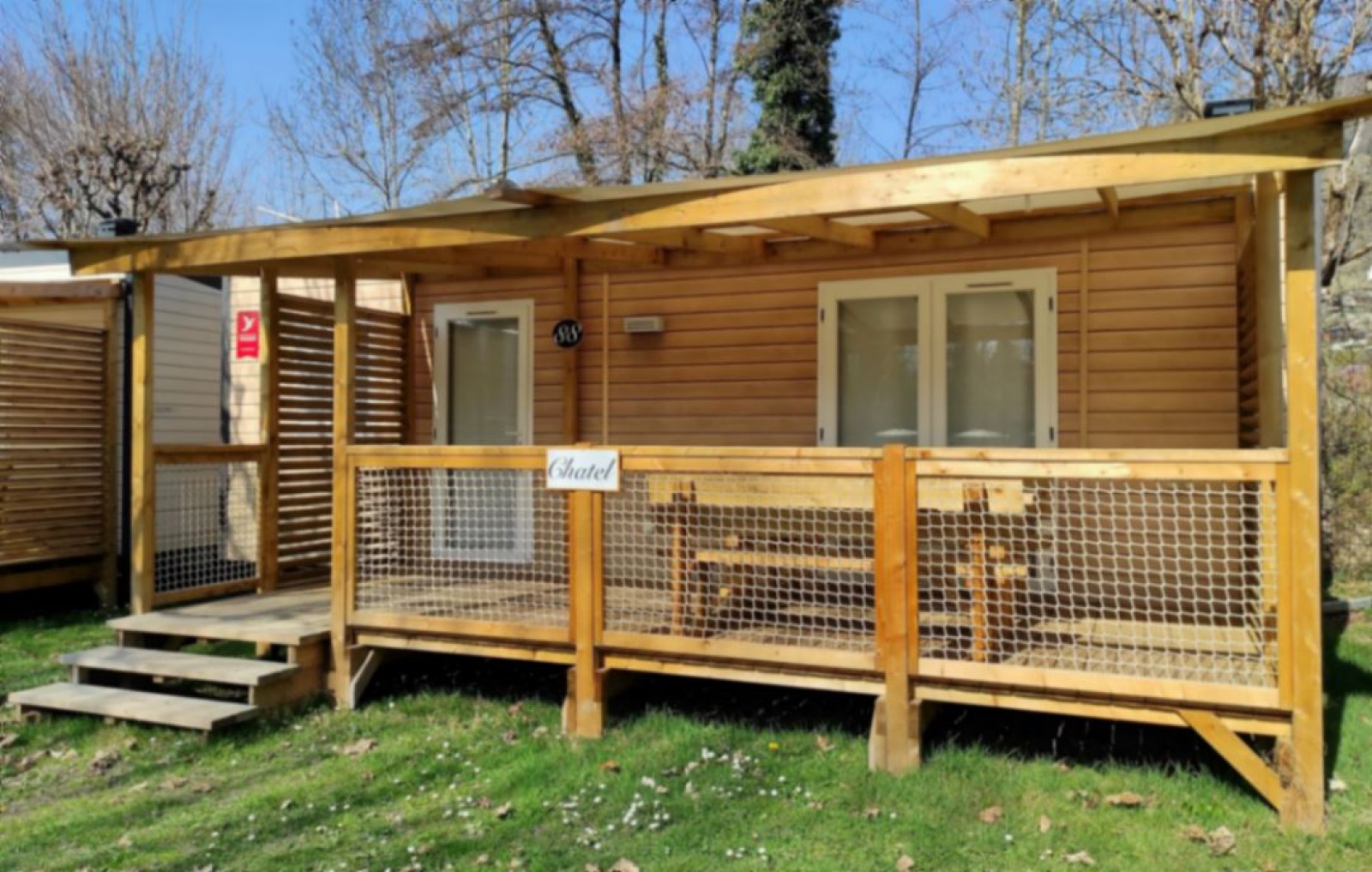 Buitenfoto van een gezellige glampinghut met houten veranda, bankje en natuur rondom het verblijf.