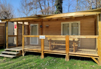 Foto exterior de una cabaña glamping acogedora con porche de madera, banco y barandilla en la naturaleza.
