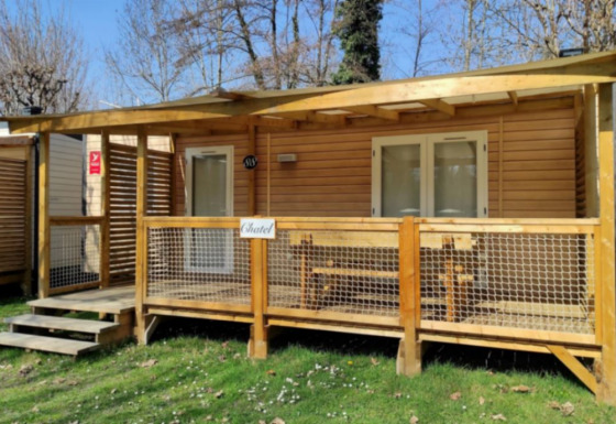 Buitenfoto van een gezellige glampinghut met houten veranda, bankje en natuur rondom het verblijf.