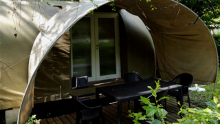 Safari tent named Coco Sweet with wooden terrace, black table and chairs surrounded by greenery.