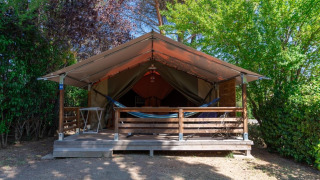 Safari tent called Freeflower without sanitary facilities, featuring a veranda and hammock surrounded by trees.
