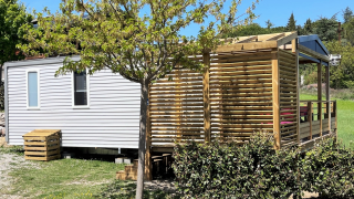 Casa mobile al Mobile Home Living Lodge con terrazza in legno, alberi e cespugli, sotto il cielo sereno.
