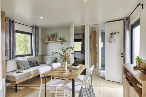 Interno moderno e accogliente di Mobile Home New Horizon con zona pranzo, divano e grandi finestre sul verde.