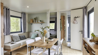 Interno moderno e accogliente di Mobile Home New Horizon con zona pranzo, divano e grandi finestre sul verde.