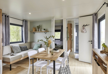 Moderne opholdsstue i Mobile Home New Horizon med spisebord, sofa og lyse trædetaljer, udsigt til natur.