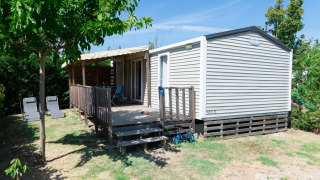 Premium Mobilheim mit 2 Schlafzimmern, Terrasse, Liegestühlen und Rollern in grünem Garten.