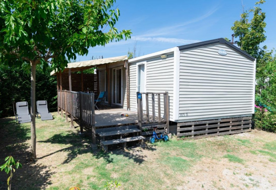 Premium Mobile Home with 2 bedrooms, terrace, lounge chairs, and scooter in a shaded garden area.
