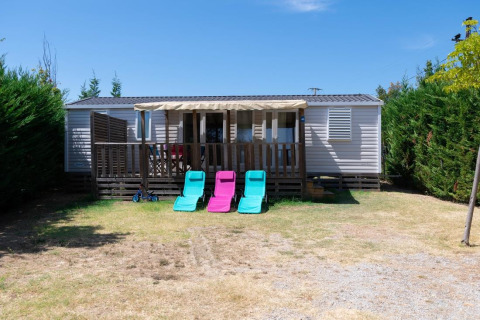 Mobil-home Premium 3 chambres, terrasse, transats et haies vertes lors d’une journée ensoleillée.
