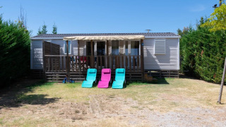 Premium Mobile Home with 3 bedrooms, porch, lounge chairs, surrounded by green hedges in sunlight.