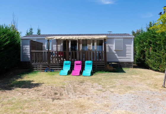 Casa mobile Premium con 3 camere da letto, veranda, sdraio e siepi verdi sotto il sole.