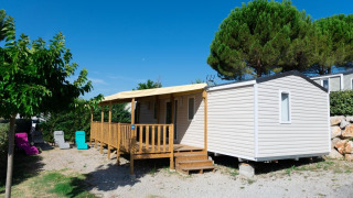 Premium Mobile Home 4 dormitorios, casa móvil moderna con terraza de madera, sillas y árboles alrededor.