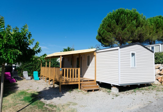 Premium Mobile Home 4 dormitorios, casa móvil moderna con terraza de madera, sillas y árboles alrededor.