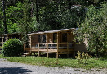 Premium Trendy mobilhome-lodge med træveranda og omgivet af grønne træer og buske i naturskønne omgivelser.