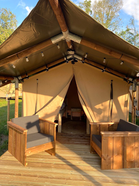 Safari tent Lodge Insolite Bivak met houten stoelen op de veranda en open ingang tijdens zonnige dag.