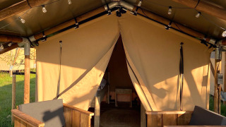 Safari tent Lodge Insolite Bivak met houten stoelen op de veranda en open ingang tijdens zonnige dag.
