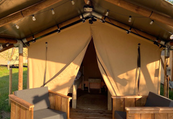 Safari tent Lodge Insolite Bivak met houten stoelen op de veranda en open ingang tijdens zonnige dag.
