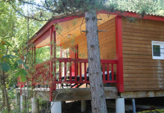 Houten chalet met rode veranda bij Flower Camping la Pinède in Frankrijk, omringd door bomen.