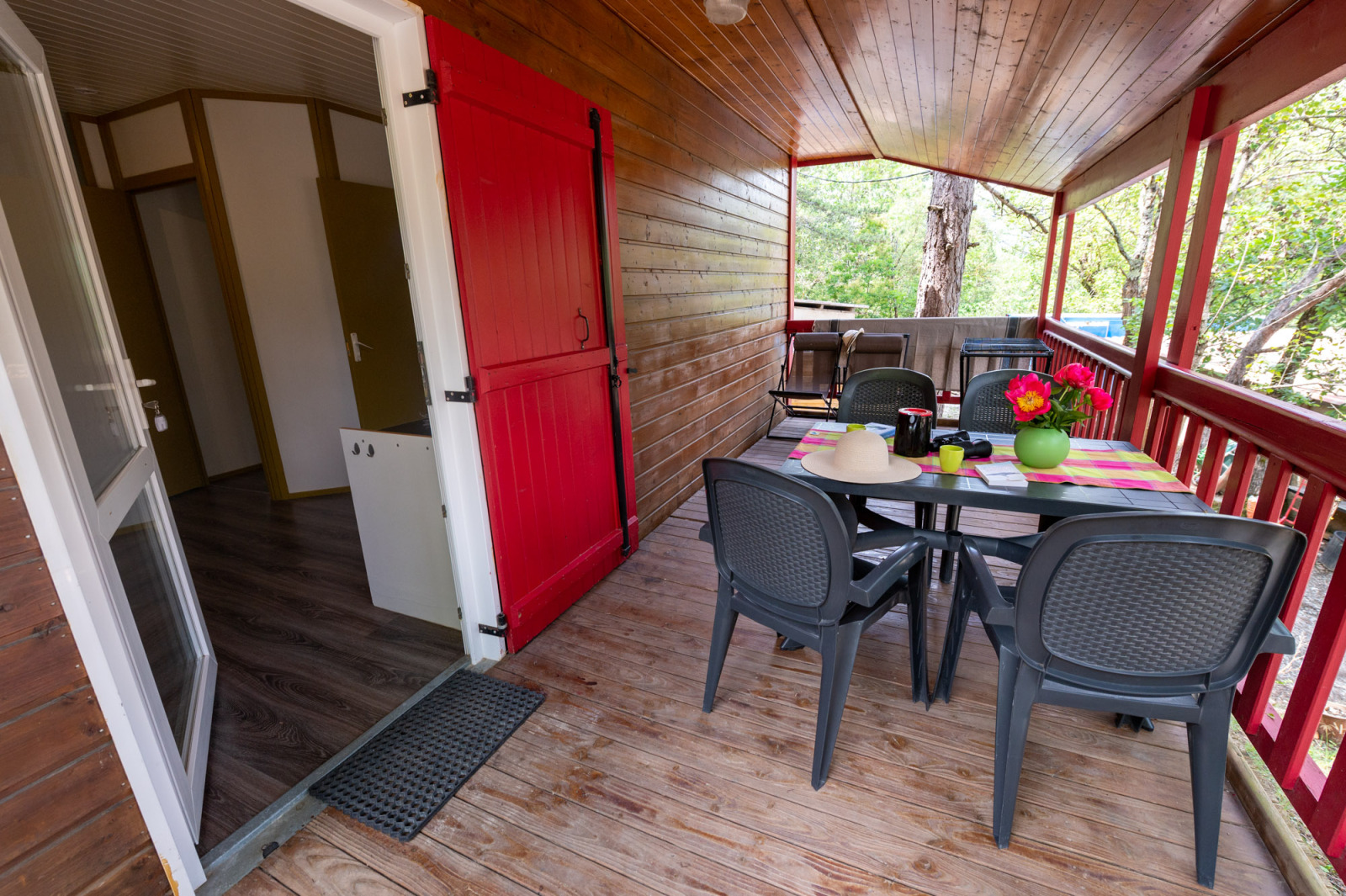 Uitzicht op een houten veranda met eettafel en plastic stoelen bij Chalet «l'O douce» bij Flower Camping la Pinède.