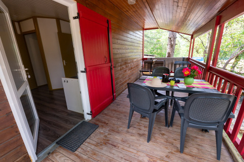 Uitzicht op een houten veranda met eettafel en plastic stoelen bij Chalet «l'O douce» bij Flower Camping la Pinède.