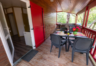 Uitzicht op een houten veranda met eettafel en plastic stoelen bij Chalet «l'O douce» bij Flower Camping la Pinède.