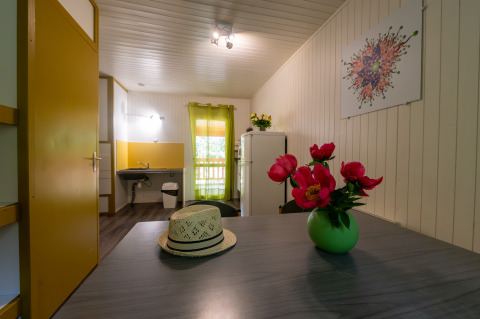 Interieur van Chalet «l'O douce» bij Flower Camping la Pinède in Frankrijk met tafel, hoed en bloemen.