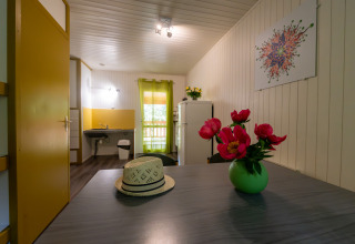Interieur van Chalet «l'O douce» bij Flower Camping la Pinède in Frankrijk met tafel, hoed en bloemen.