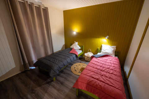 Kamer in Chalet «l'O douce» met twee eenpersoonsbedden, kleurrijke dekbedden en warme verlichting, Flower Camping la Pinède.
