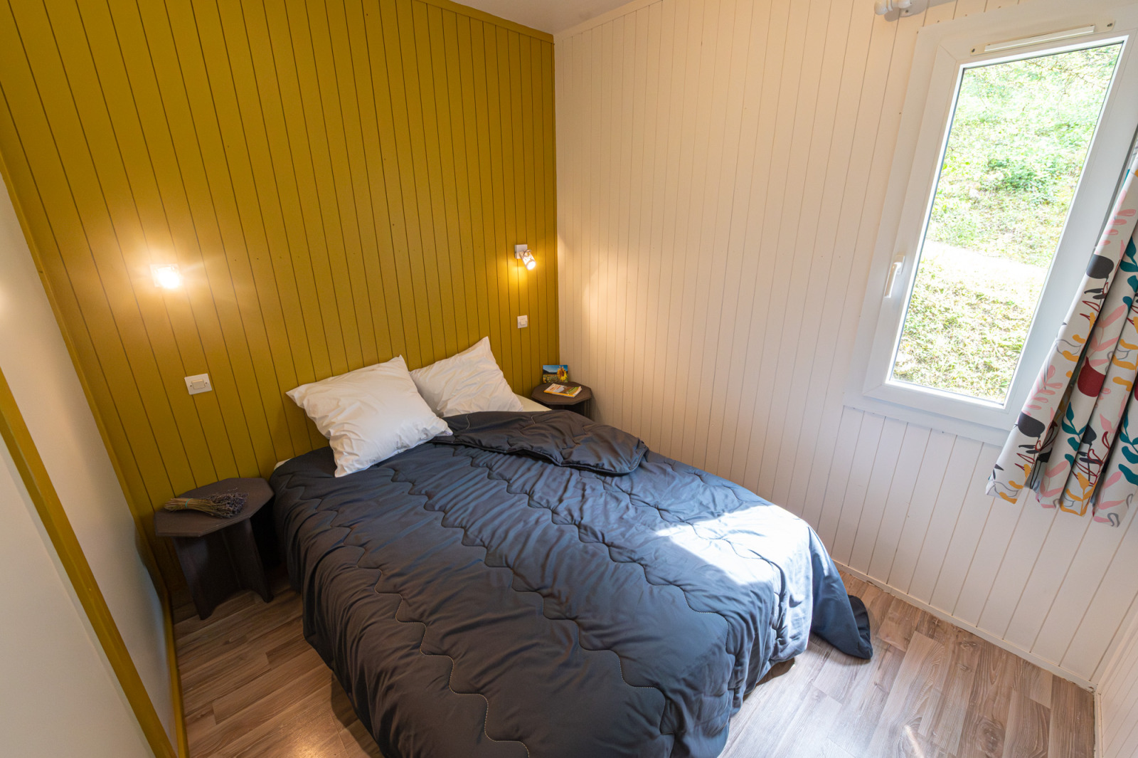 Knusse slaapkamer met tweepersoonsbed in Chalet Comfort Authentiek, Flower Camping la Pinède, Frankrijk, zonnig raam.