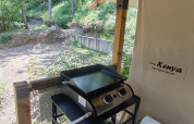 Buitenzone van safaritent met gasgrill, vuilbak en zicht op het bosrijke gebied in de achtergrond.