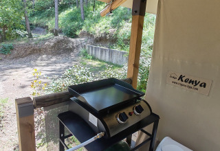 Buitenzone van safaritent met gasgrill, vuilbak en zicht op het bosrijke gebied in de achtergrond.