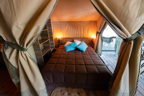 Knusse slaapkamer met tweepersoonsbed in de safaritent Lodge Insolite Pinède op Flower Camping la Pinède.