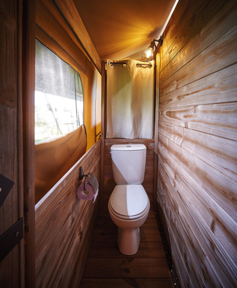 Badkamer in safaritent met houten muren, toilet, raam met hor en gordijn voor meer privacy.
