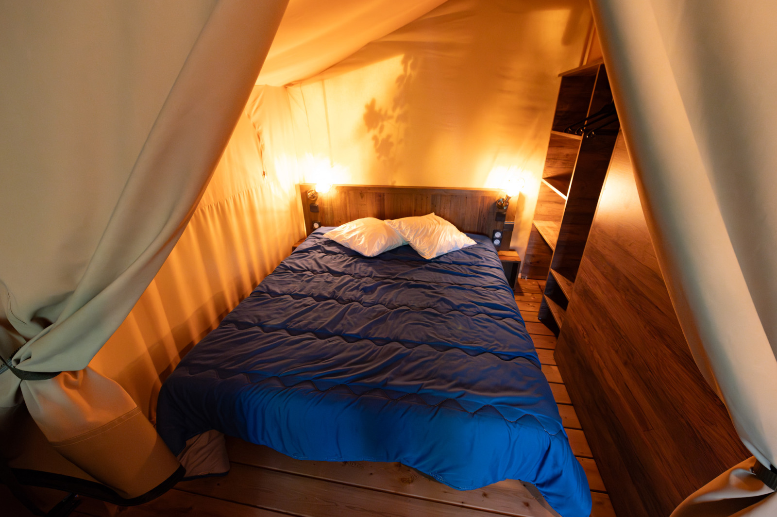 Binnenaanzicht van een safaritent met tweepersoonsbed, houten vloer en warme verlichting bij Flower Camping la Pinède.