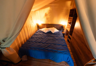 Binnenaanzicht van een safaritent met tweepersoonsbed, houten vloer en warme verlichting bij Flower Camping la Pinède.