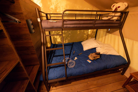 Interieur van een safaritentlodge met stapelbed, blauwe dekens en speelgoed bij Flower Camping la Pinède.