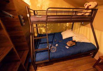 Indretning af en safari teltlodge med køjeseng, blå sengetæppe og legetøj på Flower Camping la Pinède.