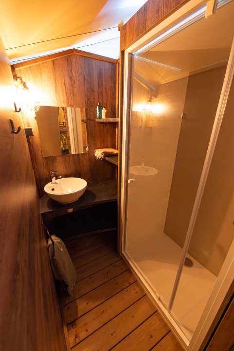 Badkamer met houten wanden, douchecabine, wastafel en spiegel in Lodge Insolite Pinède bij Flower Camping la Pinède, Frankrijk.