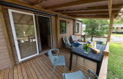 Terrasse en bois d’un lodge avec chaises, table, transats et fleurs, entourée de verdure en été.