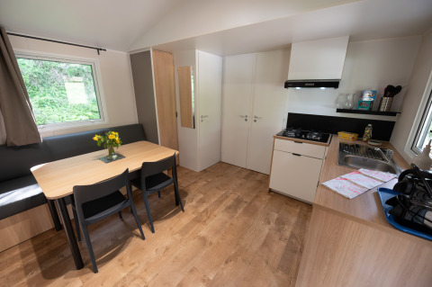 Vue intérieure d'un lodge moderne et lumineux avec table à manger, kitchenette, canapé et grandes fenêtres.