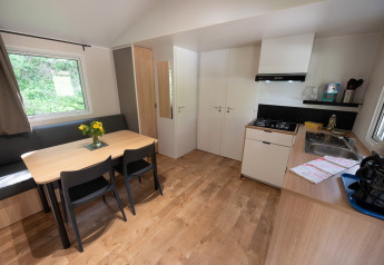 Indvendig udsigt over en moderne, lys lodge med spisebord, tekøkken, sofa og store vinduer.