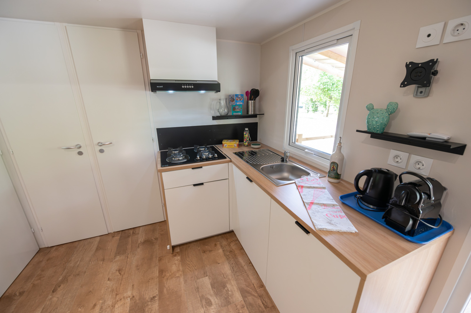 Compacte lodgekeuken met gaskookplaat, gootsteen, koffiezetapparaat, waterkoker en open planken.