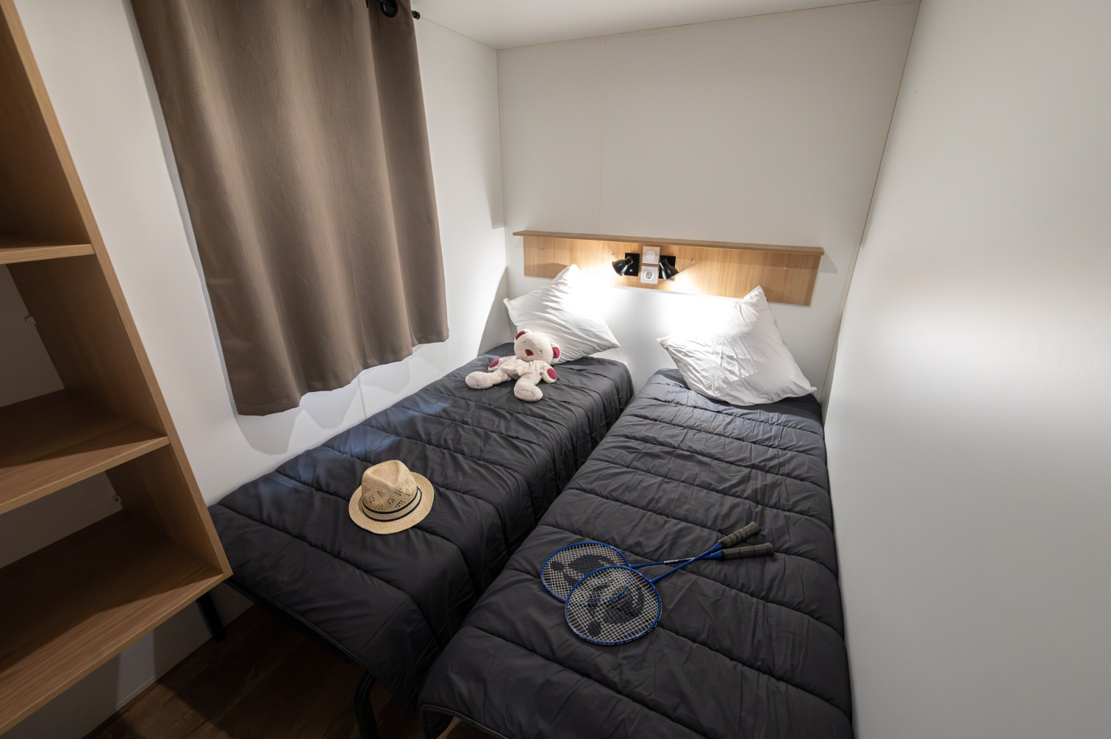 Foto van een knusse lodgekamer met twee eenpersoonsbedden, teddybeer, hoed en badmintonrackets op de bedden.