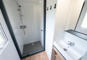 Badeværelse i en lodge med bruseniche, hvid vask, spejl, og vindue, moderne og minimalistisk design.