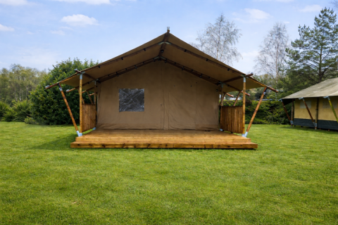 Safaritent bij Glamfield Lodge op een grasveld onder blauwe lucht, omgeven door bomen en struiken.