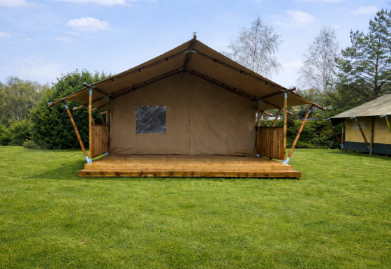 Safaritent bij Glamfield Lodge op een grasveld onder blauwe lucht, omgeven door bomen en struiken.